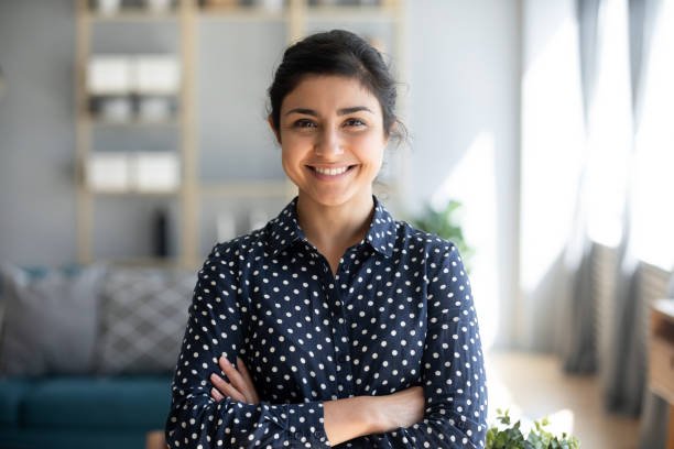 Head shot portrait smart confident smiling millennial indian woman standing with folded arms at home. Attractive young hindu teenager student girl freelancer looking at camera, posing for photo.